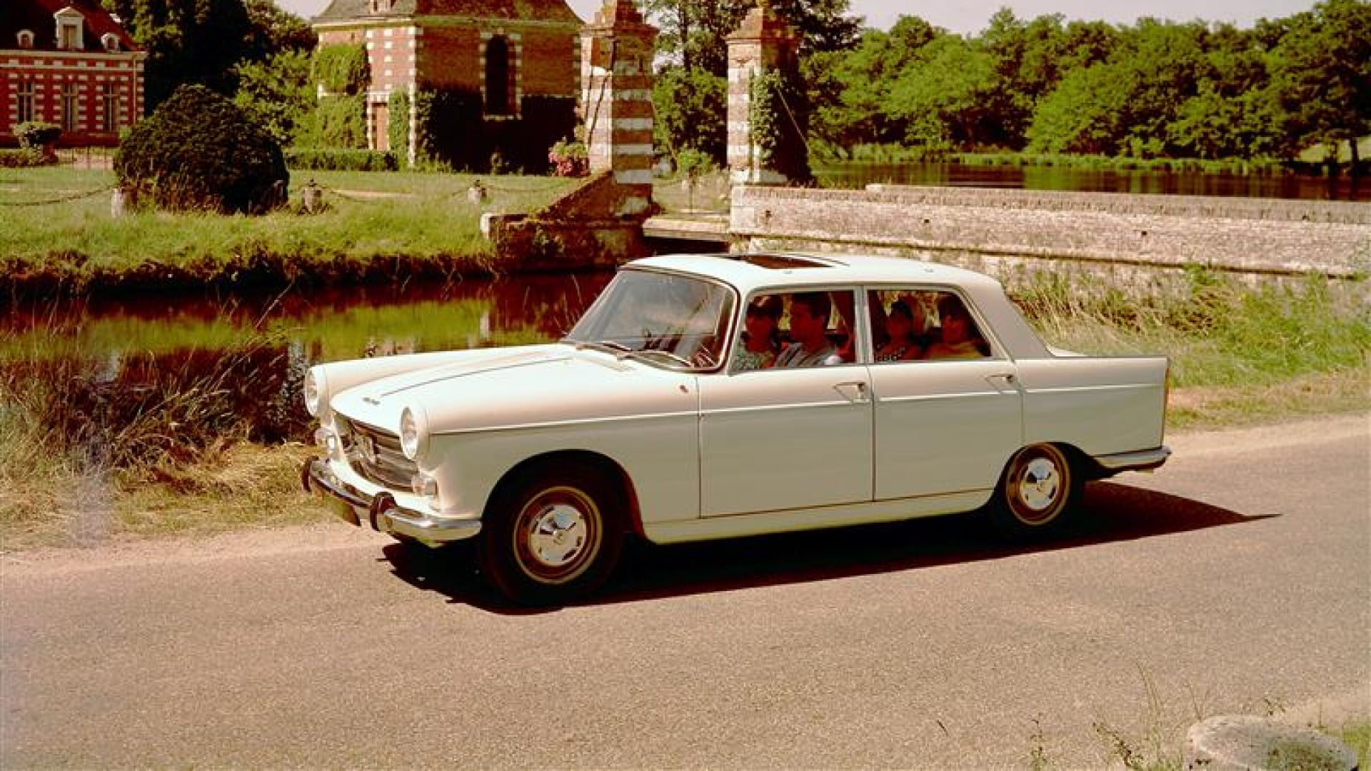 PEUGEOT 404 en una carretera rural frente a un castillo de ladrillo rojo y vegetación